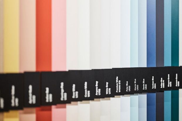 Close-up of a neatly arranged collection of vertical colour and material swatches, ranging from warm yellows, reds, pinks and neutrals to cool blues and dark tones. Black labeled tabs identify the different samples. The image is a product or material sample presentation rather than a room interior.