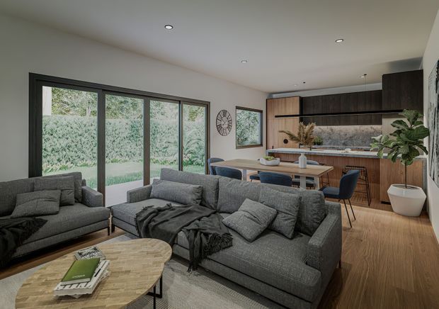 Open-plan contemporary living and dining area with a compact kitchen at the rear. The room features grey upholstered sofas, a timber oval coffee table, a timber dining table with dark upholstered chairs, dark timber kitchen cabinetry, a pale stone-look benchtop, black-framed floor-to-ceiling glazing, and light timber flooring. Large windows overlook greenery, creating a calm, refined interior.