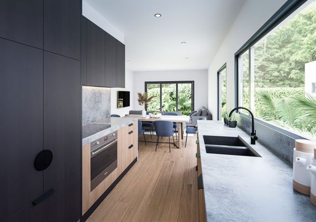 A bright, contemporary open-plan kitchen and dining area. The kitchen features dark floor-to-ceiling cabinetry, pale timber lower cabinetry, a light stone benchtop and splashback, integrated appliances, a black gooseneck tap, and a deep double-bowl sink. Full-height glazing brings in abundant natural light and overlooks lush greenery. A dining table and chairs sit beyond the kitchen, with a living area visible in the background.
