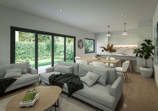 A bright open-plan living and dining area with a contemporary kitchen at the rear. The room features grey upholstered sofas, a light timber oval coffee table, pale timber flooring, white cabinetry, a stone-look kitchen benchtop and splashback, black-framed full-height glazing, pendant lights, recessed ceiling lights, and leafy garden views.
