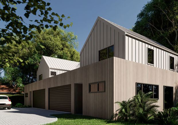 Exterior view of a contemporary multi-level residence with two steeply pitched gable volumes clad in vertically ribbed light grey panels. The lower level includes two dark garage doors, a pedestrian entry, and large black-framed windows, while mature trees and planted garden beds surround a pale paved driveway.