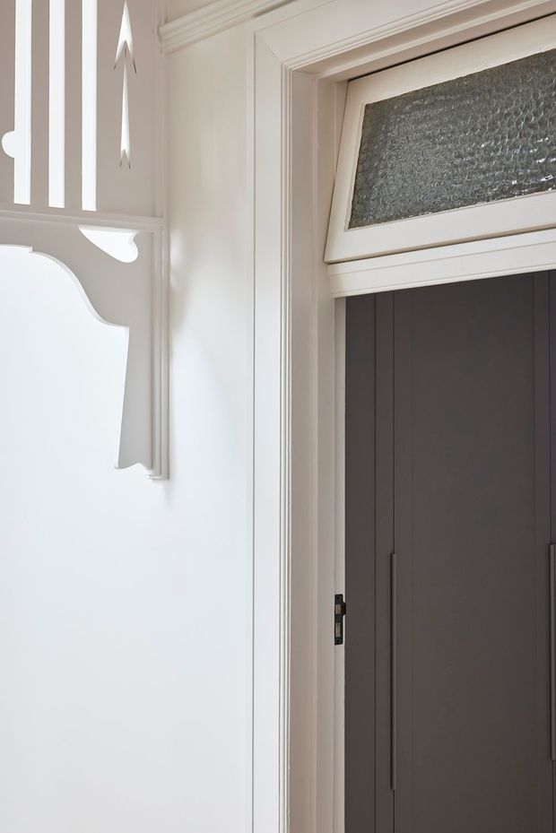 Close-up interior view of a refined entryway featuring a dark double door with slim vertical handles, surrounded by white painted trim and ornate decorative wall panelling. A textured glass transom window sits above the door, while the adjacent wall includes carved traditional detailing and a partially visible decorative mirror or panel.