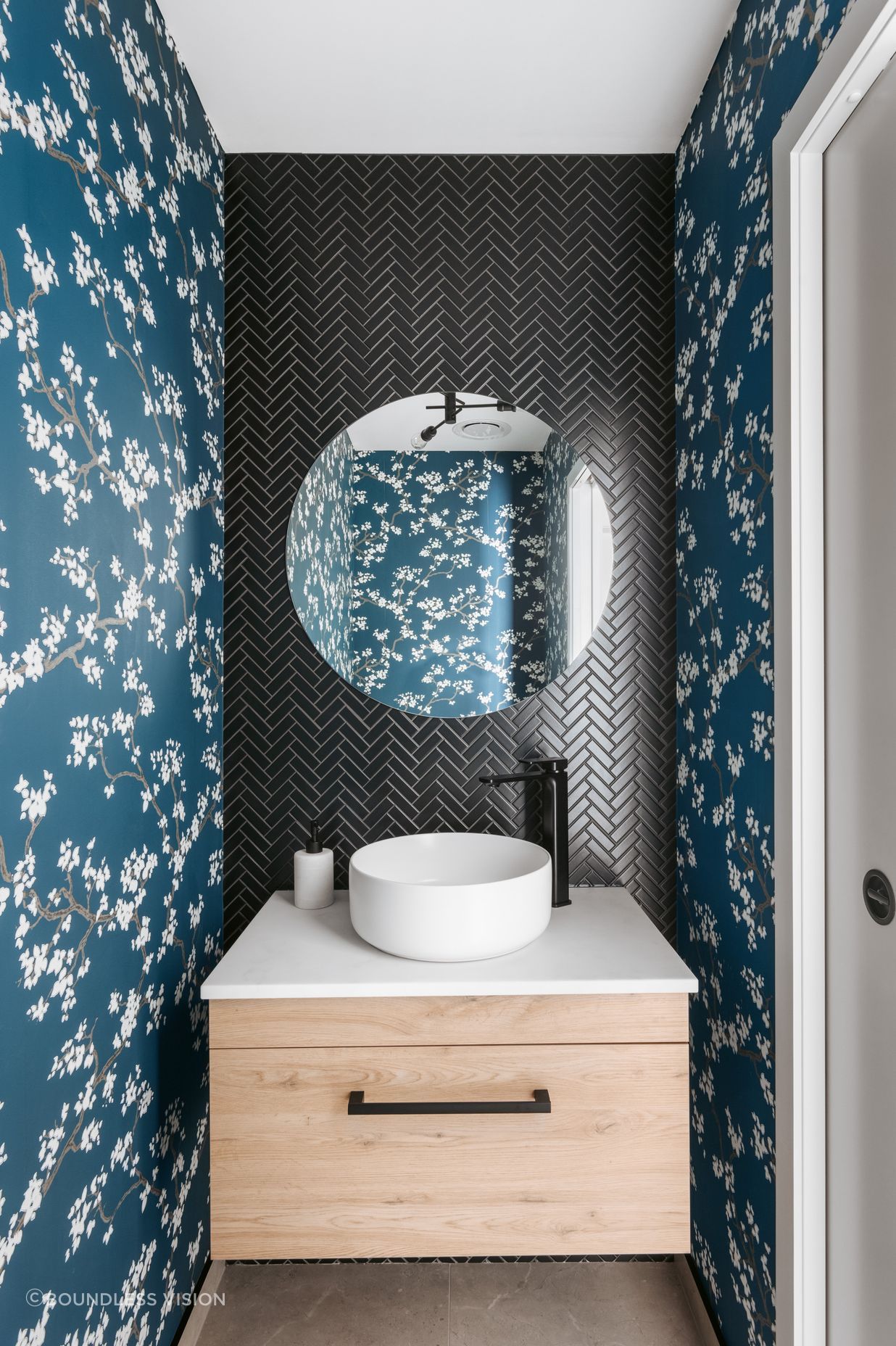 The guest powder room delights with its black herringbone tiles and cherry blossom covered wallpaper.
