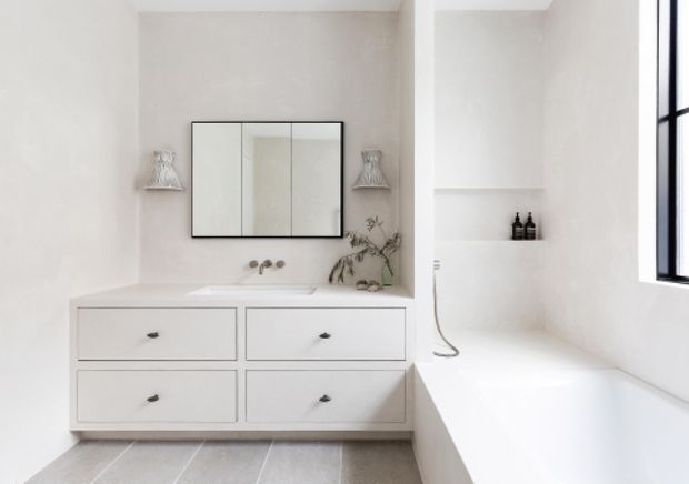Bright minimalist bathroom featuring a floating double-drawer vanity, wall-mounted taps, mirrored cabinet, freestanding bathtub, recessed shelf, and black-framed window. The space uses a restrained white and light-grey palette with subtle decorative styling.