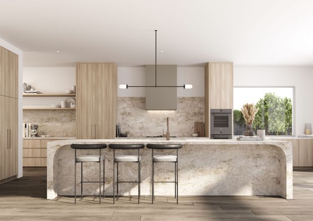 Contemporary open-plan kitchen featuring a large waterfall-edge stone island with integrated seating, light timber cabinetry, open shelving, built-in appliances, and a linear pendant light. A textured stone backsplash and island create a warm, natural focal point, with garden greenery visible through the window.