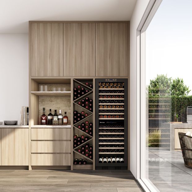 Contemporary built-in wine storage wall with light timber cabinetry, open bottle shelving, drawers, a wine display rack, and a refrigerated wine cellar. The space opens through large glazed doors to an outdoor terrace, with pale timber-look flooring and neutral finishes.