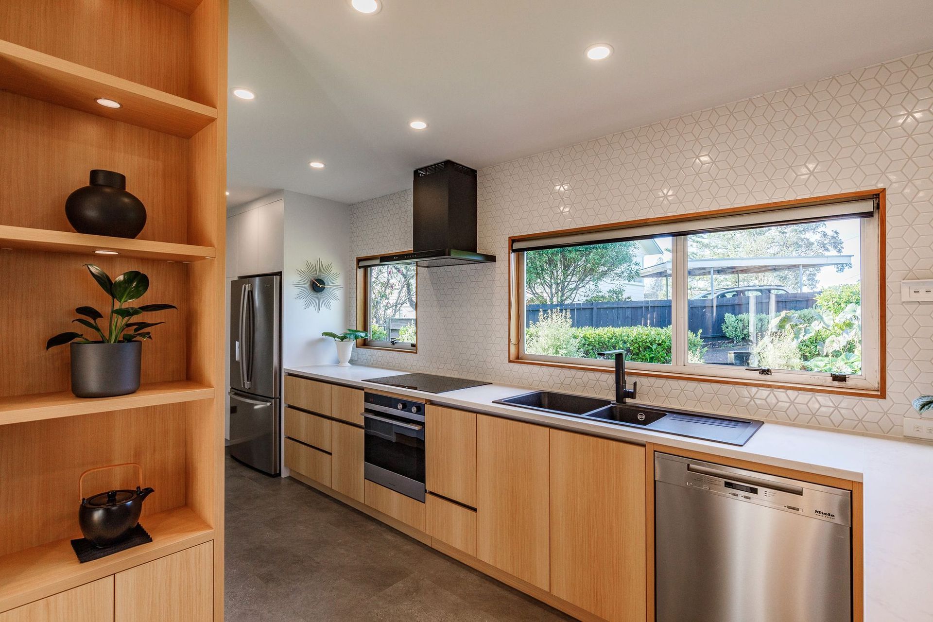 The blend of wood, white, and black accents creates a timeless and inviting ambiance, while the textured splashback tiles add subtle interest.