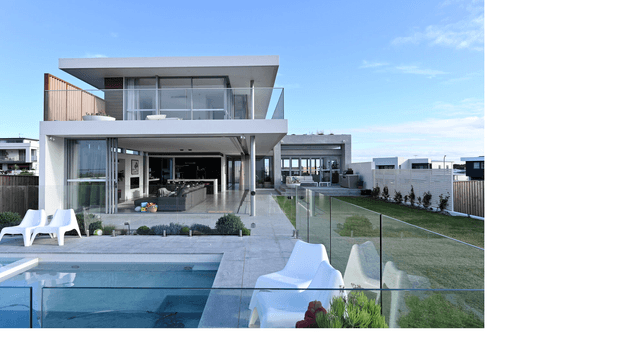 Exterior view of a contemporary multi-level residence with broad roof overhangs, extensive floor-to-ceiling glazing, concrete-toned surfaces, and a glass balustrade. The home opens onto a paved terrace and rectangular swimming pool, with a landscaped lawn and outdoor seating. The scene is bright and open with a clean, modern architectural composition.