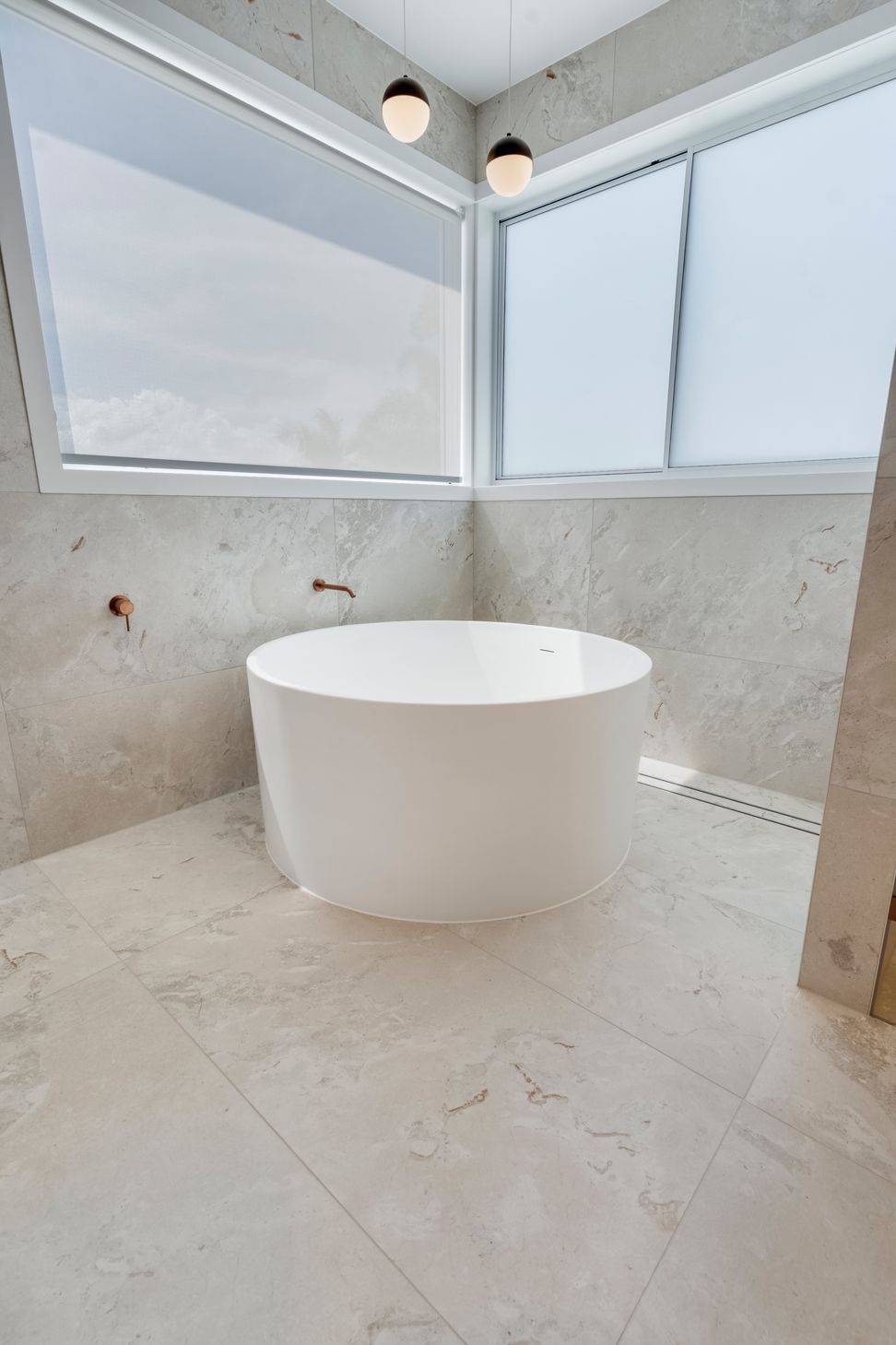 Round mirrored cabinets and brass pendants give the dual vanity its considered symmetry.