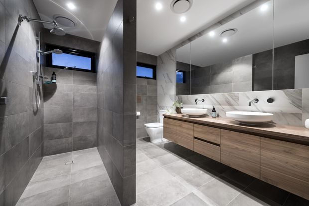 Contemporary bathroom with a large walk-in tiled shower, double vessel basins, wall-to-wall mirror, floating timber vanity, recessed lighting, and narrow high windows. The space uses large-format grey tiles with a marble-look splashback and warm wood joinery.