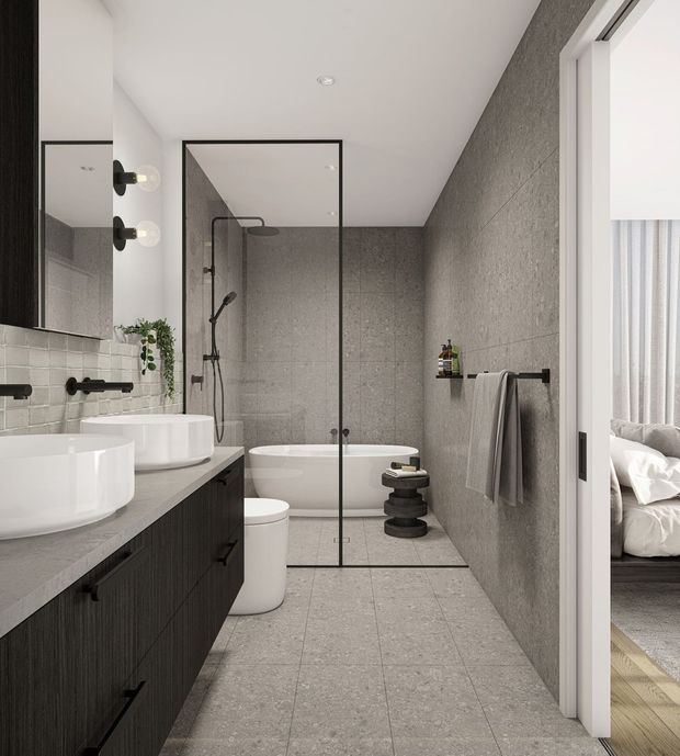 Contemporary bathroom with a long dark timber vanity, twin white vessel basins, black tapware, large grey stone-look wall and floor tiles, a freestanding bathtub, and a black-framed glass shower enclosure. A bedroom is visible through the open doorway on the right.