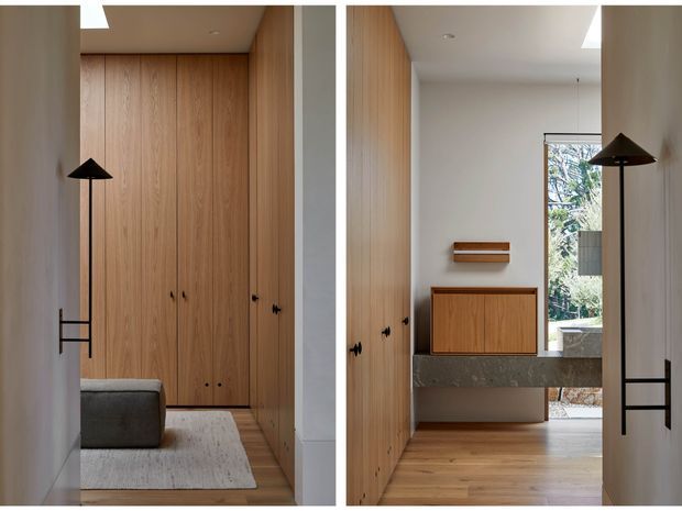 Diptych view of a refined residential entryway or hallway with full-height natural timber built-in cabinetry, matching timber flooring, white walls, and minimalist black wall-mounted lamps. The right-hand view shows a floating timber console and a substantial grey stone ledge beneath a narrow wall shelf, with daylight entering through a glazed opening to an outdoor area. The space is clean-lined, warm, and understated.