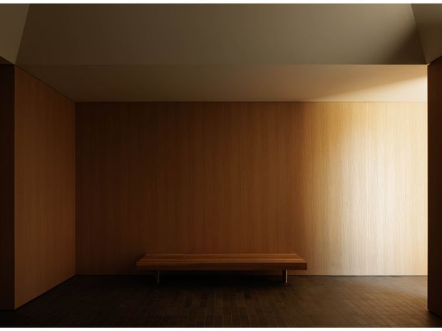 A minimalist enclosed seating alcove or entry-like space with richly timber-lined walls, a dark timber floor, and a simple built-in timber bench. Warm directional lighting highlights the right wall while the remaining surfaces recede into shadow.
