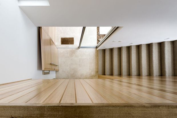 Upside-down architectural interior view of a contemporary stairway and landing. Pale timber stair treads and flooring dominate the foreground, with a textured neutral carpeted stair run along the right, light wood wall panelling and cabinetry at the far end, and a skylight or glazed ceiling opening bringing in natural light.