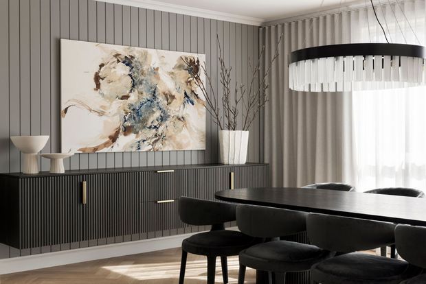 Refined contemporary dining room featuring a dark fluted wall and matching ribbed sideboard, a large abstract artwork, a dark dining table with upholstered chairs, and a striking circular pendant light. Sheer curtains soften the bright window, while sculptural ceramics and branches add understated decoration.