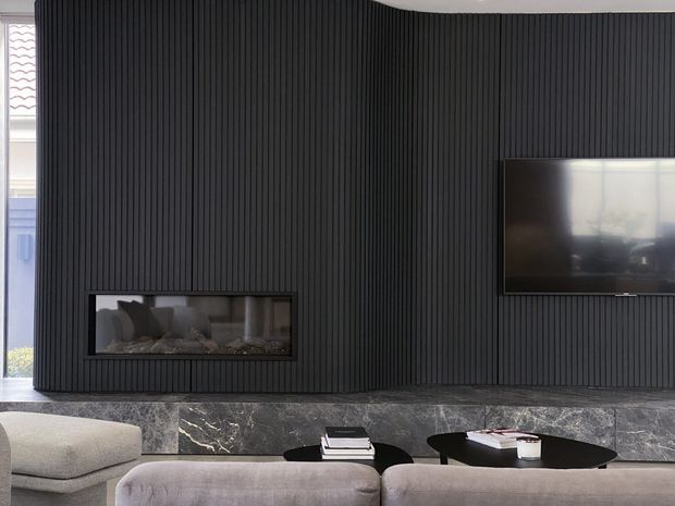 Contemporary living room dominated by a dark vertical-ribbed feature wall with a built-in linear fireplace and wall-mounted television. A dark stone hearth runs beneath the wall, while neutral upholstered seating and low black coffee tables create a refined, high-contrast interior.