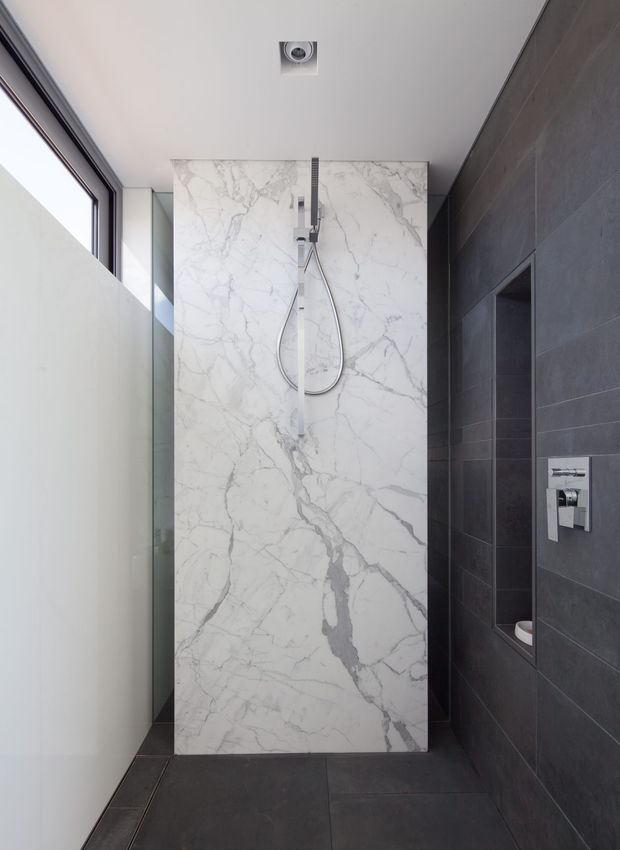 Contemporary walk-in shower with a large white marble-look feature slab and wall-mounted shower fittings. Dark charcoal tiled walls and floor create a strong contrast, with a recessed wall niche and a narrow glazed opening providing natural light.