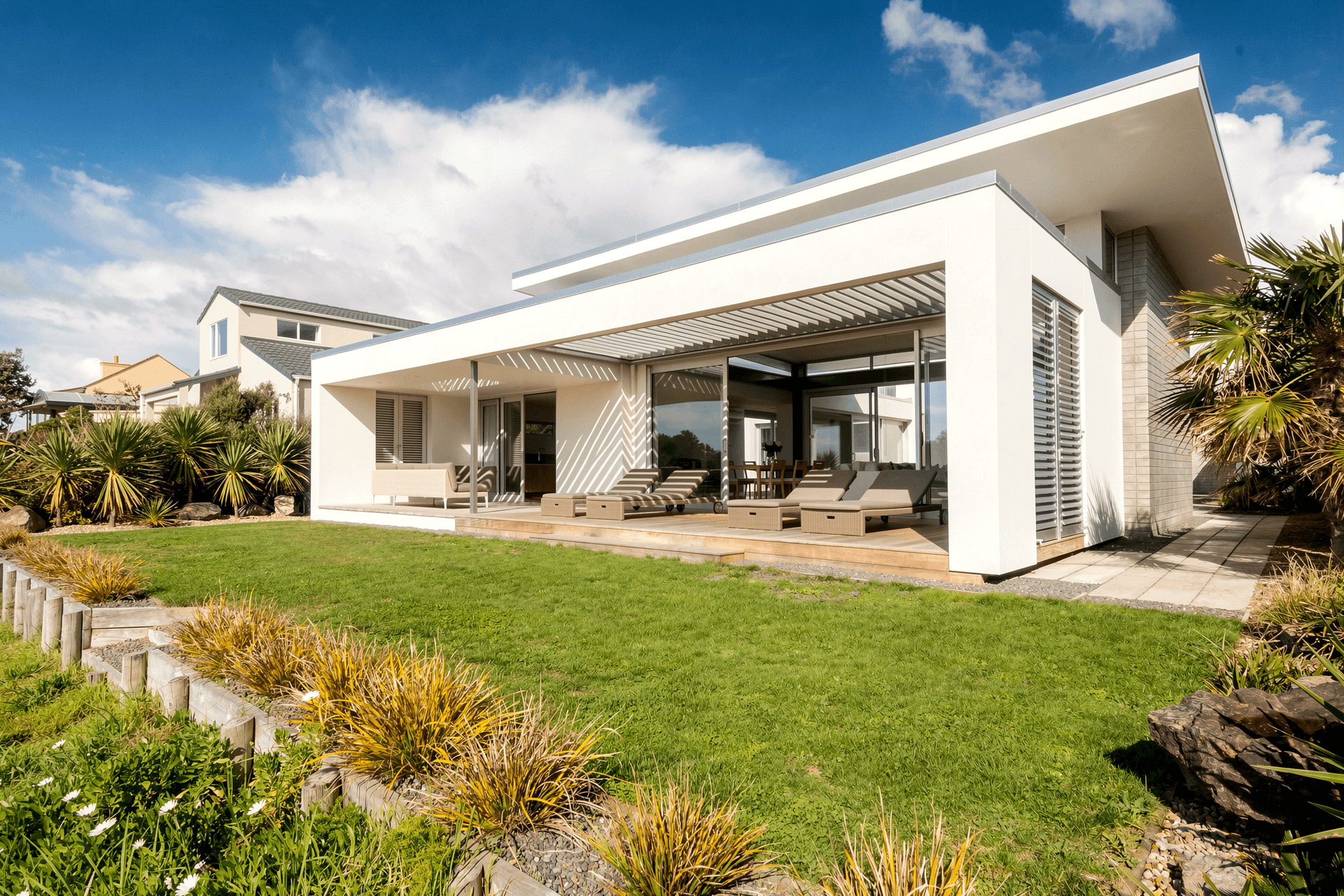 Viewed from the corner of the site, the long, low form of the house stretches across the beachfront. Expansive glazing and a sheltered deck connect the open-plan interiors directly to the lawn, sand dunes and coastal landscape.