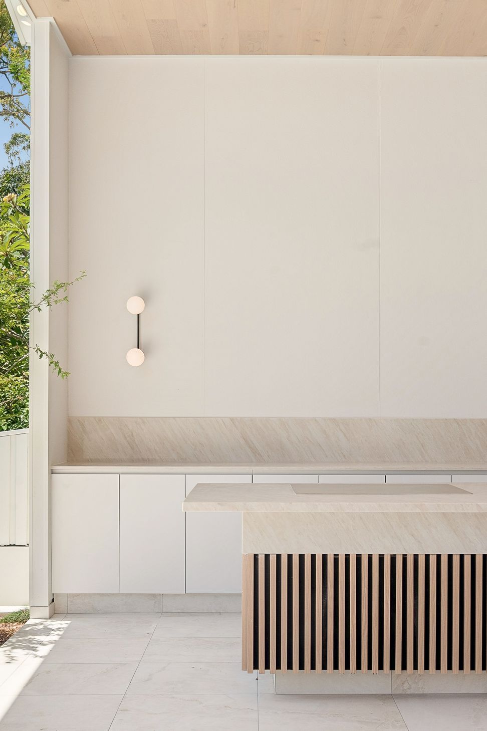 A slim wall light picks out the timber slat screen beside the outdoor cabinetry.