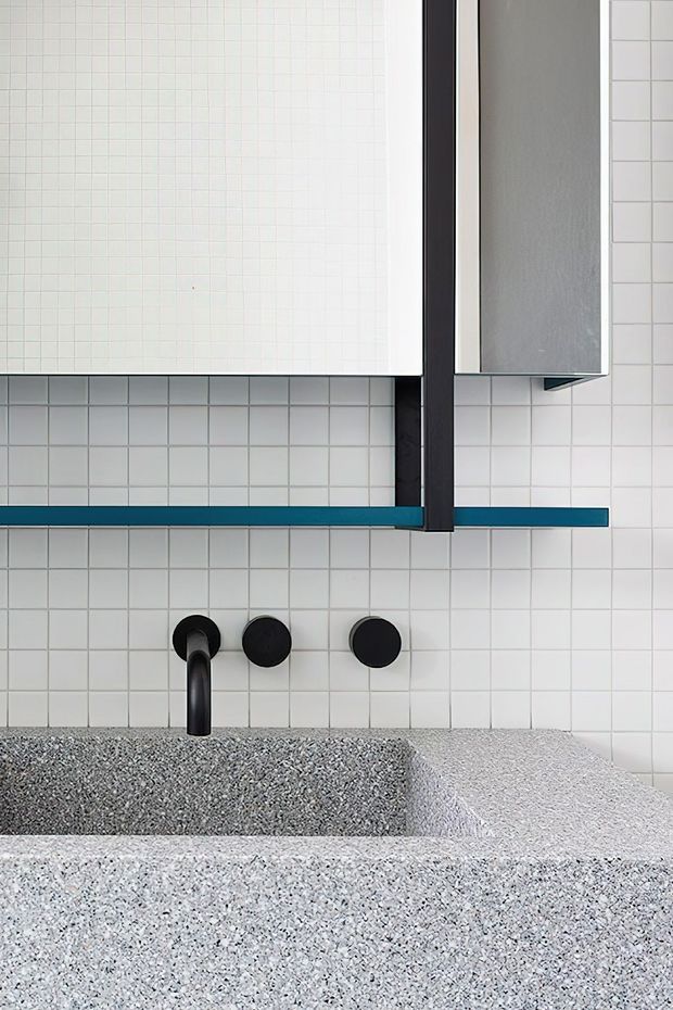 Close-up of a contemporary bathroom vanity featuring a white square-tile wall, a speckled terrazzo basin and benchtop, matte black wall-mounted tapware, and a black-framed mirrored cabinet with a narrow teal shelf accent.