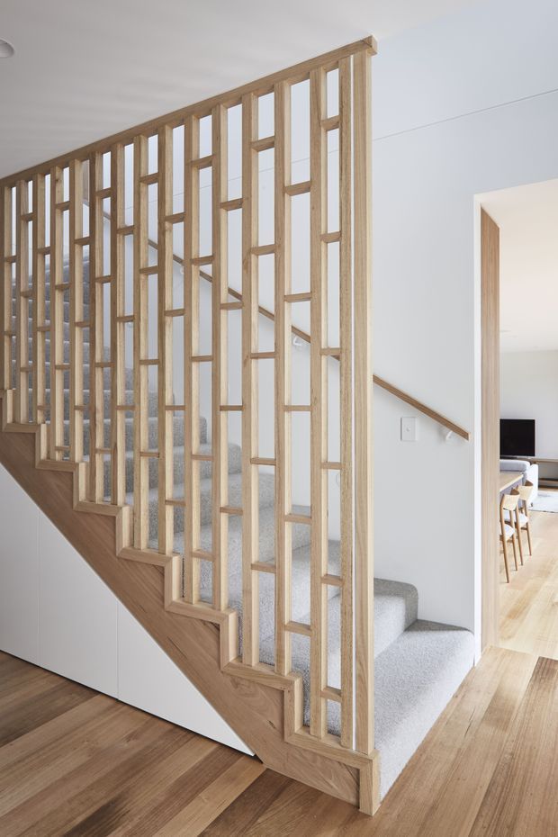 Bright contemporary interior featuring a staircase with grey carpeted steps, a light timber stringer and floor, and a distinctive open timber stair balustrade composed of vertical and horizontal slats. A hallway and dining area are visible beyond the stairwell.