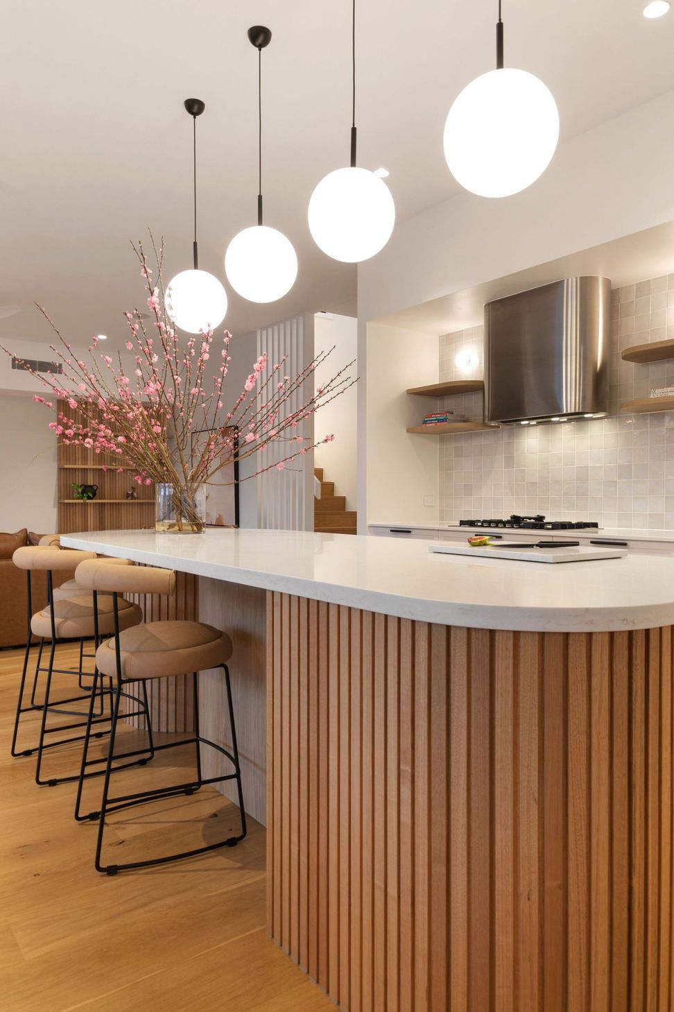 The island curves to soften the room — marble over fluted timber, with zellige behind the cooktop.