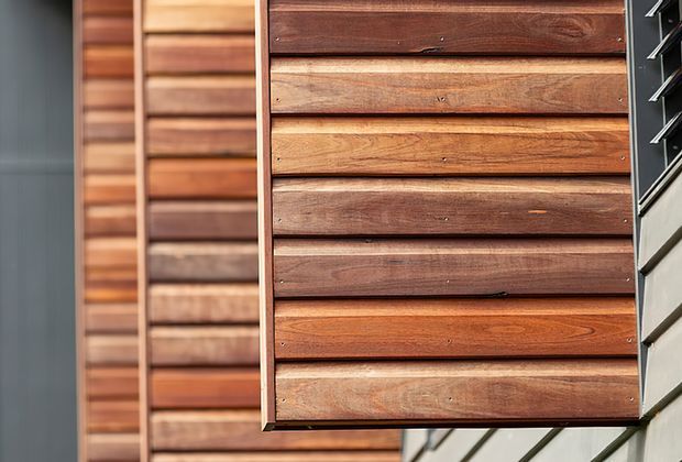 Close-up exterior detail of a building facade featuring horizontal timber weatherboard cladding in varied warm brown tones, with a projecting timber-clad box or panel and contrasting light grey cladding visible at the right edge.