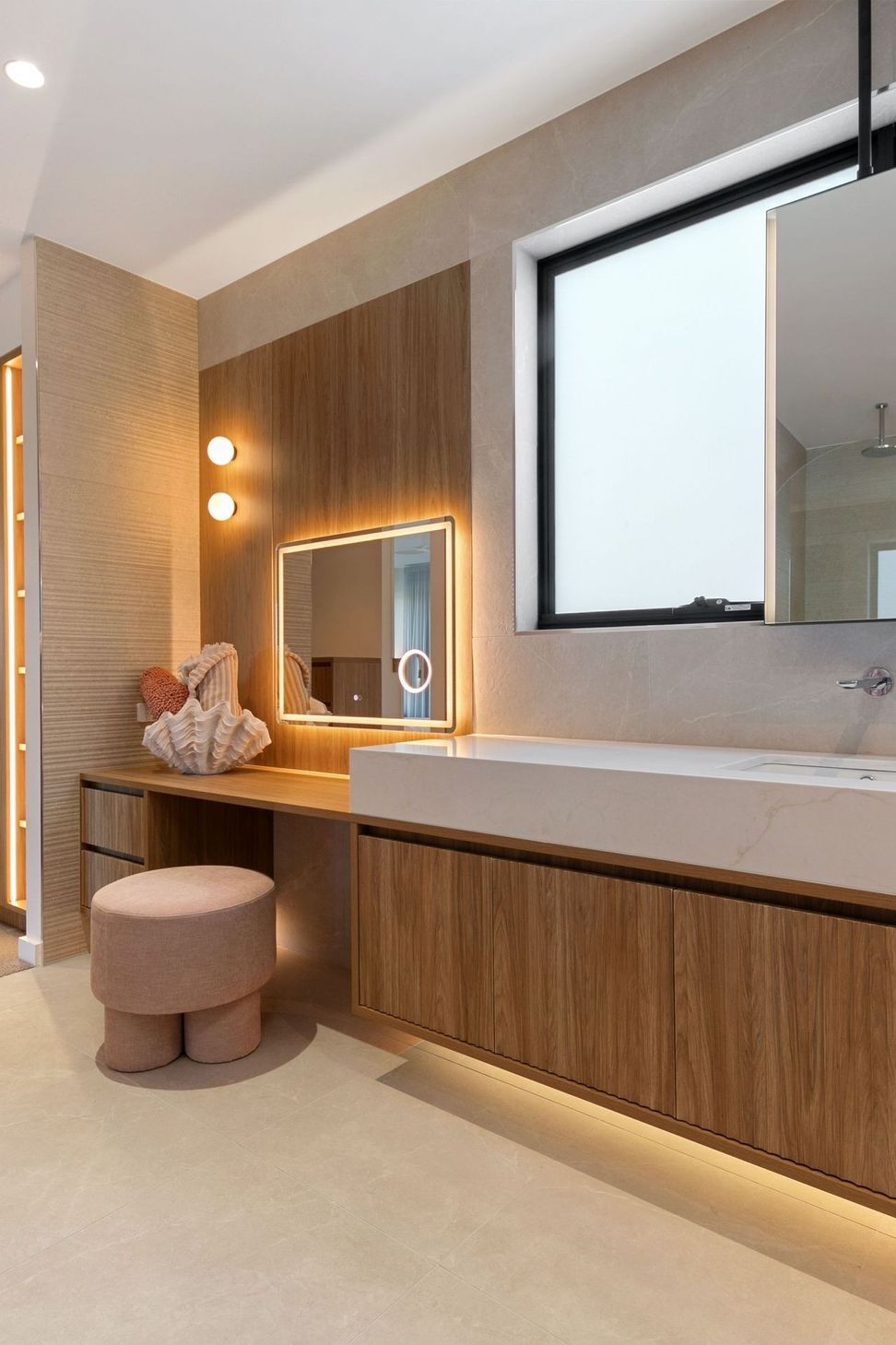 The ensuite pairs walnut with stone, lit from behind for softness.