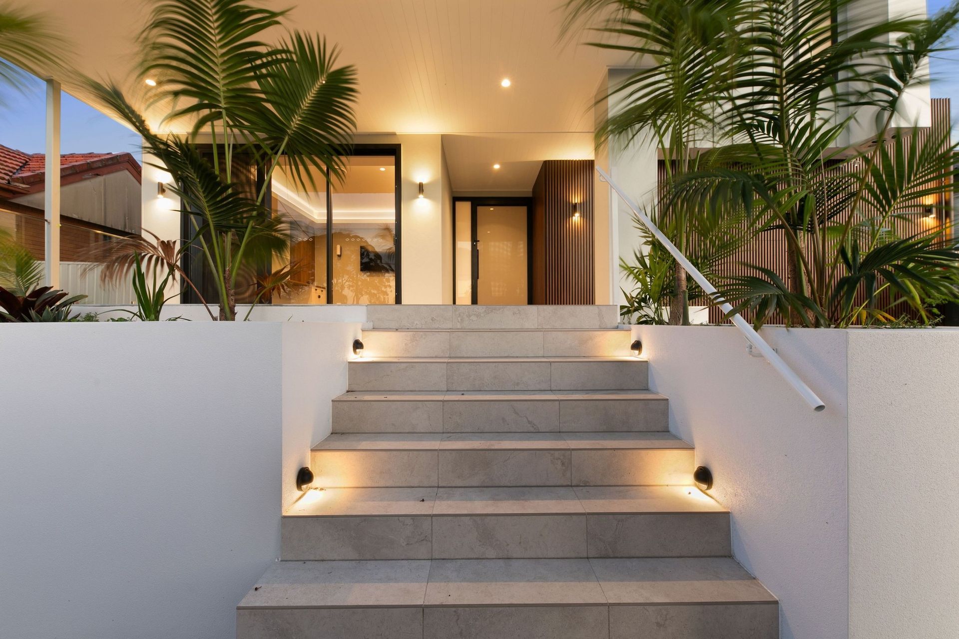 Layered lighting and tropical planting turn arrival into a sequence, stepping up to the front door.