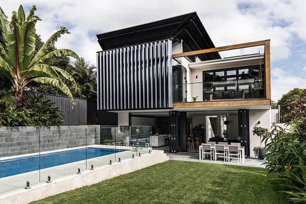Contemporary multi-level residence with bold black and white architectural detailing, vertical louvres, timber-framed upper balcony, extensive glazing, and a landscaped backyard with a swimming pool, glass pool fencing, and outdoor dining area.