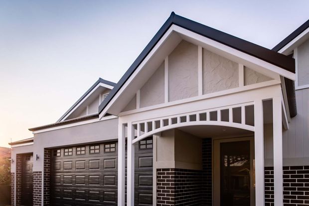 Exterior view of a multi-gabled suburban home featuring a prominent front entry porch, dark paneled garage doors, white rendered gable walls, white trim, and dark brickwork to the lower facade and columns. The design combines traditional gable proportions with clean contemporary detailing.