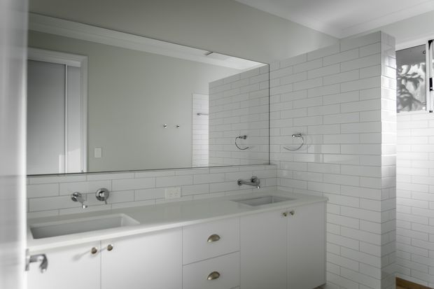 Bright, compact contemporary bathroom with a long white vanity, integrated basins, chrome tapware, large wall mirror, and white subway-tile wall finish. The restrained monochromatic palette creates a clean, practical feel.