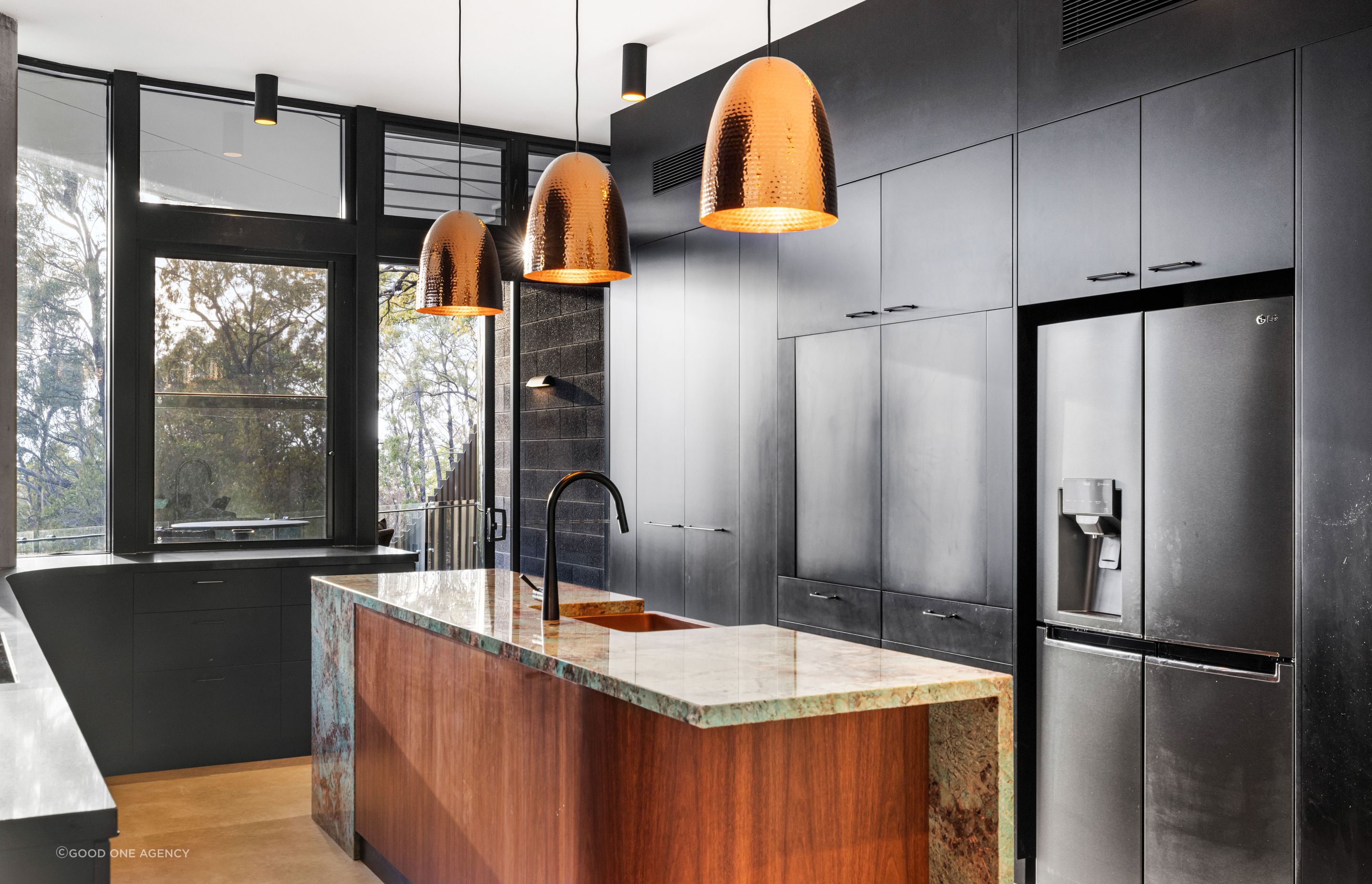 The dark cabinetry in the kitchen, contrasts against the timber veneer kitchen island and copper pendant lights.